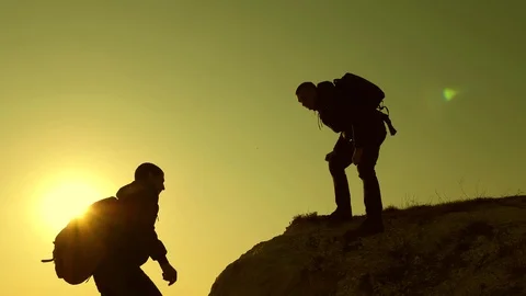 Climbers silhouettes stretch their hands to each other, climbing to top of hill Stock Footage