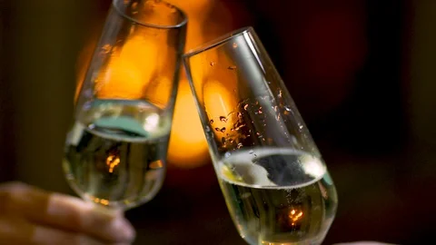 Clinking champagne glasses with warm orange fireplace on background slow motion Stock Footage
