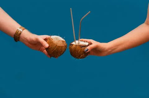 Clinking coconuts with drinking straws. Summer concept. Blue background Stock Photos
