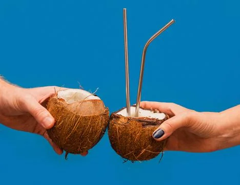 Clinking coconuts with drinking straws. Summer concept. Blue background Stock Photos