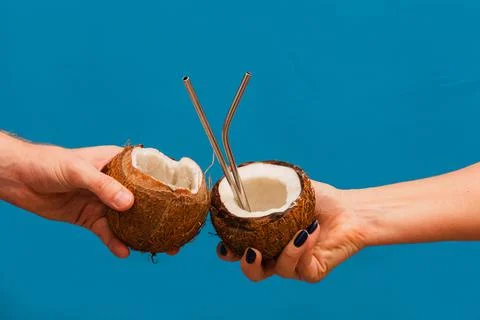 Clinking coconuts with drinking straws. Summer concept. Blue background Stock Photos
