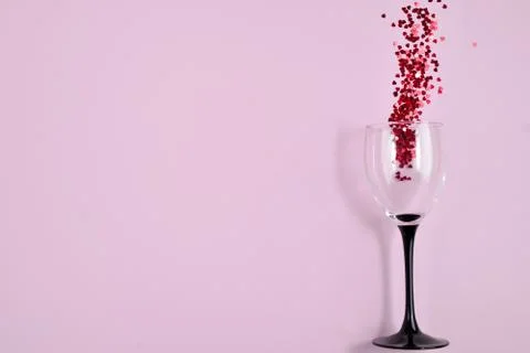 Clinking wine glasses with splash of red heart shaped confetti Foto stock
