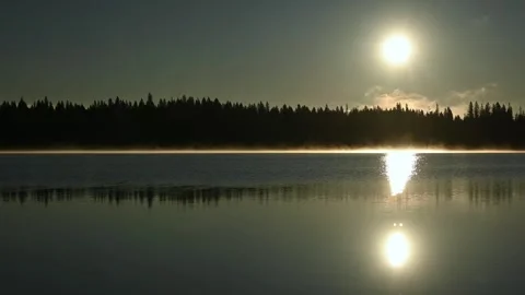 Clip looking at the sun just after sunrise. The sun is above a calm lake Stock Footage 252834911