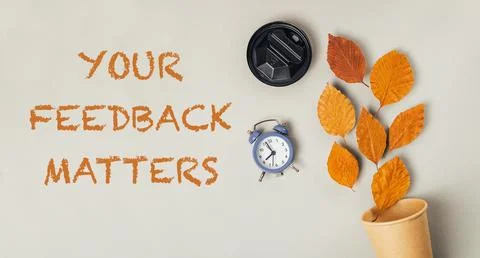 A clock and a cup are on a table with the words Your feedback matters written Stock Photos