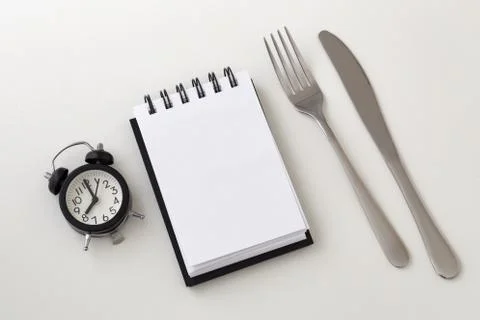 Clock and notepad with fork and knife, intermittent fasting and weight loss p Stock Photos