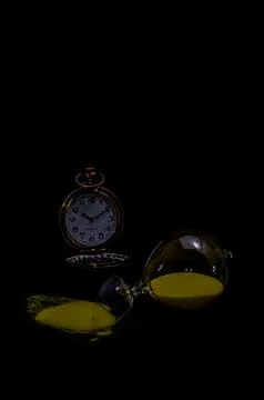 A clock and a sand timer are on a black background Stock Photos