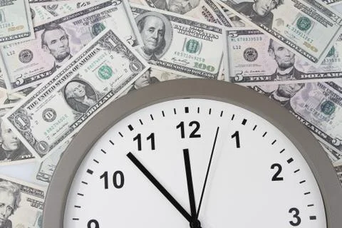 Clock on assorted American banknotes. Time is money idea Stock Photos
