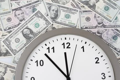 Clock on assorted American banknotes. Time is money idea Stock Photos