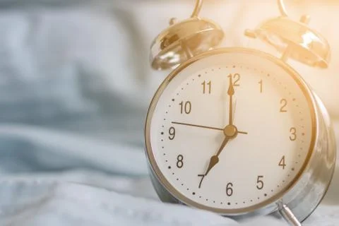 Clock on the bed in the morning. Stock Photos