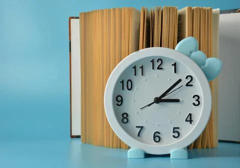 Clock with a bow on the background of an open book. Blue background. Stock Photos