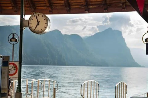 Clock in focus over the dock at vitznau with the lake &amp; a mountain range in t Stock Photos