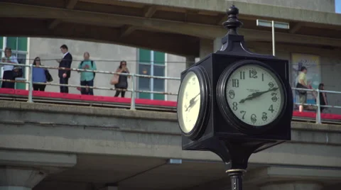 Clock in foreground with commuters waiting on a train station Stock Footage 65384296
