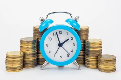 Clock in the foreground, stacks of coins in the background Stock Photos