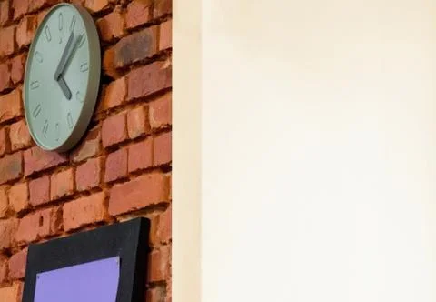 A clock with hands hangs on a rough brick wall. Another corner surface is fin 库存照片