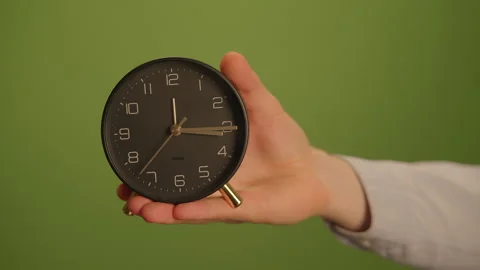 A Clock Held in Hand Set Against a Striking Green Background, Emphasizing Stock Footage 293646318