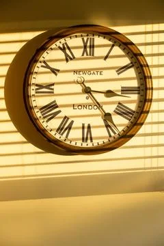 A clock on a house wall at sunset with the shadow of venetian blinds. Stock Photos