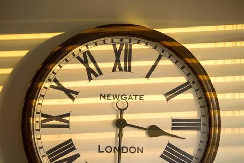 A clock on a house wall at sunset with the shadow of venetian blinds. Stock Photos