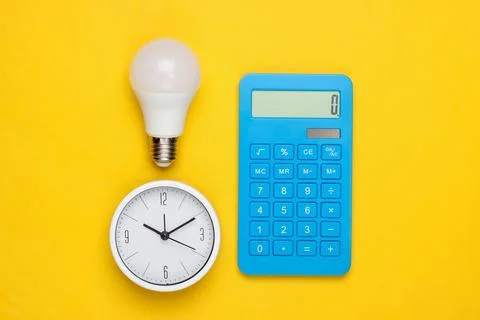 Clock with light bulb, calculator on a yellow background. Minimalism. Top vie Фото
