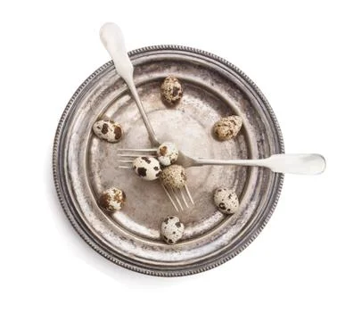 Clock made of quail eggs on silver plate with forks, isolated on white backgr Stock Photos