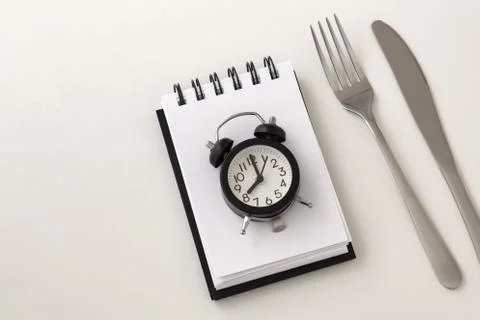 Clock on notepad with fork and knife for intermittent fasting and weight loss Stock Photos