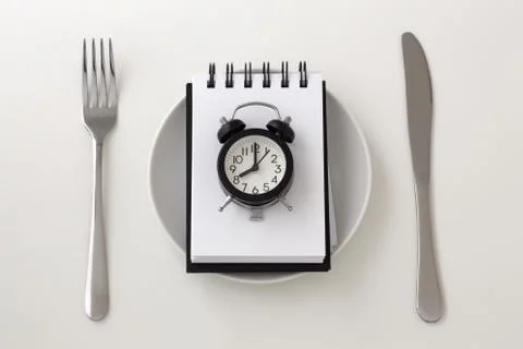 Clock on notepad with fork and knife, intermittent fasting and weight loss pl Stock Photos