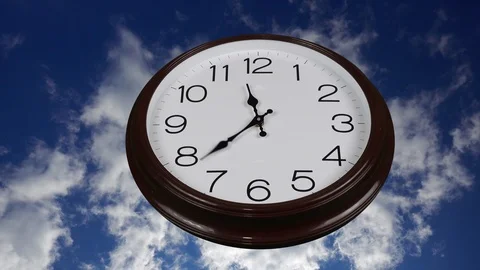 Clock with a round dial against a blue sky with clouds. Time concept. The han Stock Footage 93436022