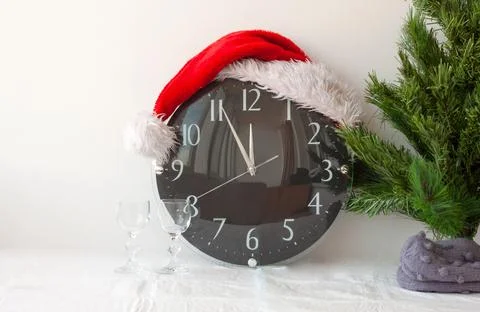 A clock in a Santa Claus hat next to an artificial Christmas tree and two gla Foto stock