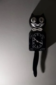 A clock shaped like a cat hangs on a wall. Stock Photos