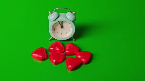 Clock shows time beside red heart shapes on green background in close-up Stock Footage 338405935