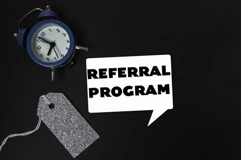 A clock is on a table with a tag that says referral program Stock Photos
