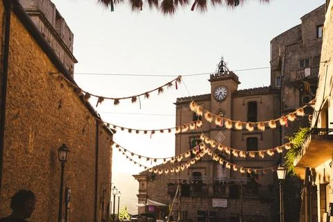 Clock tower and hanging decorations in Italian village square at sunset Stock Photos