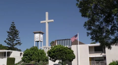 Clock tower flag in strong wind and church cross on a blue sky with trees. Video stock 67523041