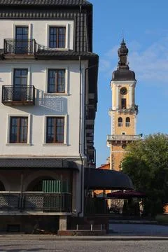 Clock tower stands tall next to building in a quiet town square during daytime Stock Photos