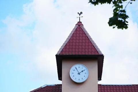 A clock tower topped with a weather vane in the shape of a rooster Stock Photos