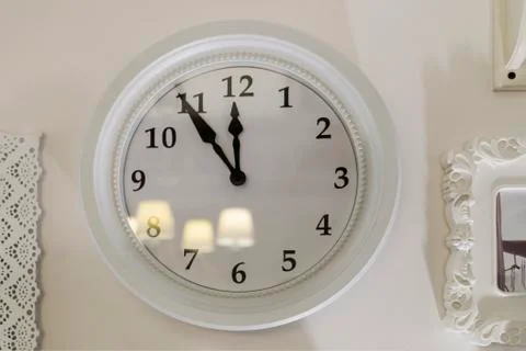 The clock on the wall is white. Eleven hours and fifty-five minutes. Stock Photos