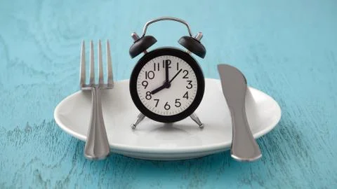 Clock on white plate with fork and knife, intermittent fasting, meal plan, we 库存照片