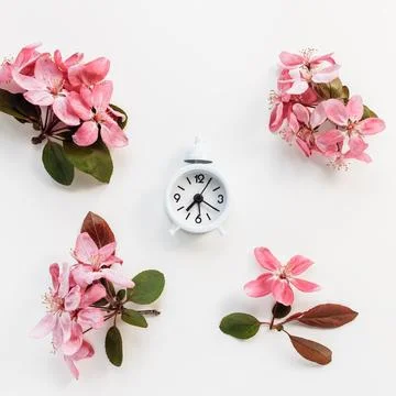 Clock on white with spring flowers background. Spring forward, daylight saving Stock Photos