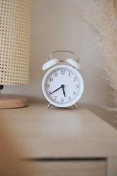 Clock on a wooden bedside table with a lamp in a cozy room Stock Photos