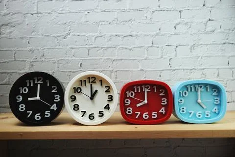 Clocks with time zone of different country on wooden shelves and white brick  库存照片