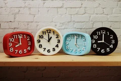 Clocks with time zone of different country on wooden shelves and white brick  库存照片