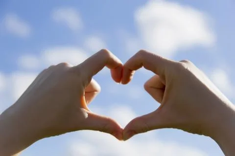 Close up of 2 hands create heart shape. Bright blue sky in the background con Stock Photos