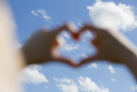Close up of 2 hands create heart shape. Bright blue sky in the background con Stock Photos