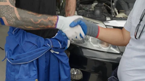 Close up of 2 mechanic hands in gloves making handshake in front of a car Stock Footage 246117989