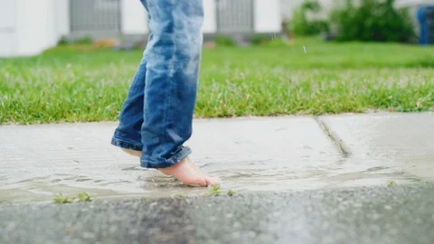Close on 2 year old boy's feet and jeans as he splashes in gutter on rainy day Vídeo Stock 127546170