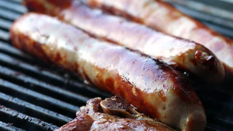 Close-up of 3 sausages and a slice of meat on a grill. The sausages are sizzling Stock Footage 163050920