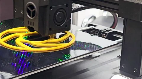 Close-up of 3D Printer Head Extruding Yellow Plastic Filament to Create a Shape Stockbeeldmateriaal 338056121