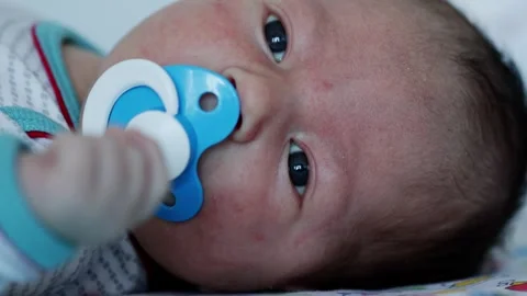 Close-up of a 5 month old caucasian babys face with a blue pacifier in his mouth Stockbeeldmateriaal 296578534