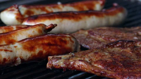 Close-up of 5 sausages and two slices of meat on a grill. The sausages are Stock Footage 163051097