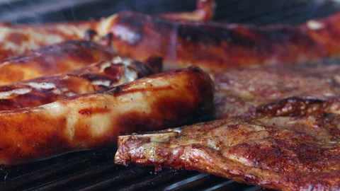 Close-up of 5 sausages and two slices of meat on a grill. The sausages are Stock Footage 163051287