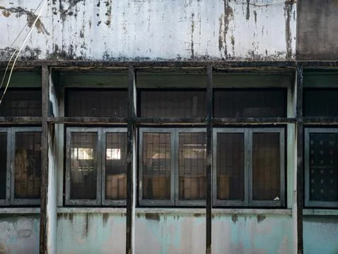 Close-up of abandoned building facade with dark grid windows, peeling paint.. Foto stock